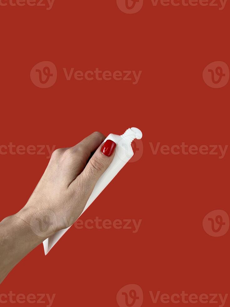 A woman is holding a tube with toothpaste on a red background. Dental care photo