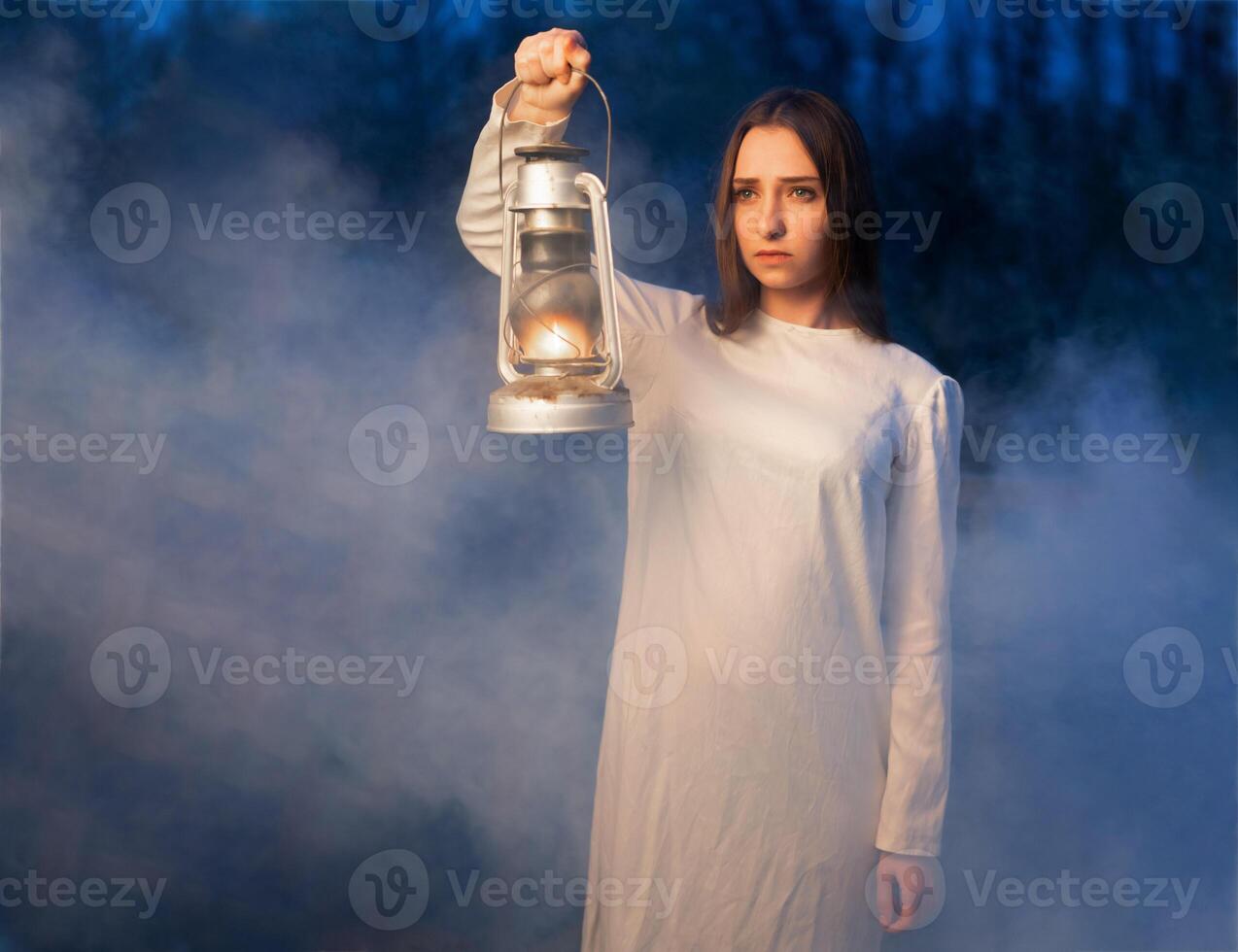 Mysterious mystical girl in a dark night forest with a kerosene lamp in her hands photo