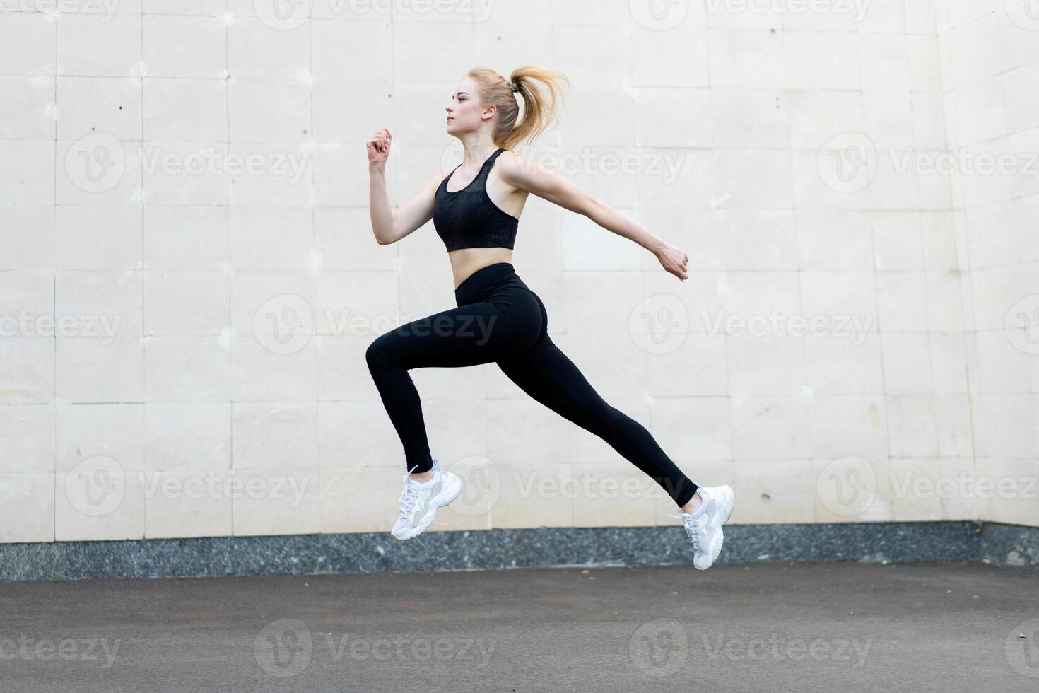 Sport and Fitness Concept Young Adult Caucasian Female Athlete Jumping High Outdoor Gray Tail Wall Background photo