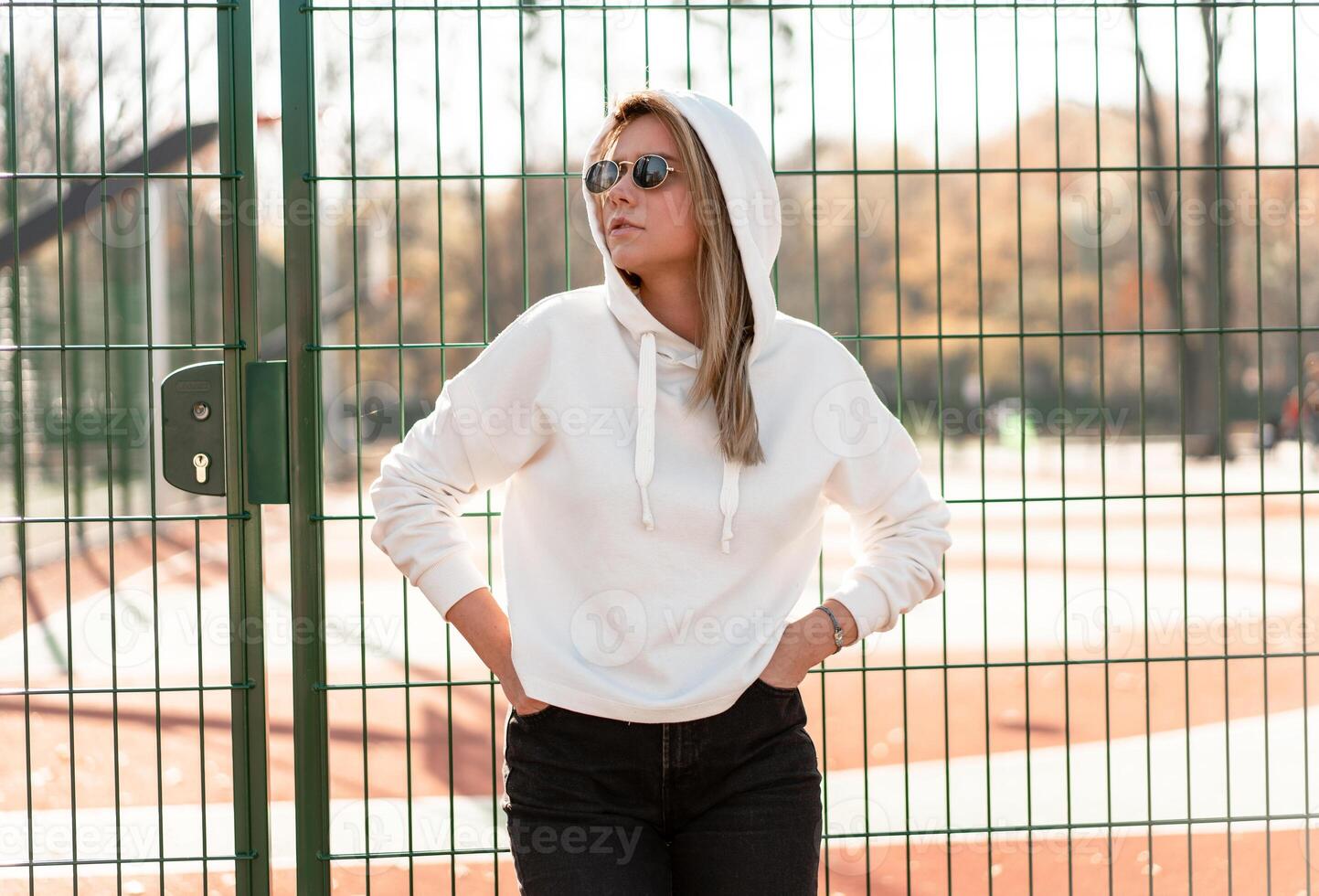 Outdoor close up portrait of young beautiful woman with long hair in sunglasses, dressed in a white sweater, near the sportsground photo