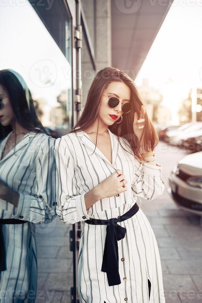Summer sunny lifestyle fashion portrait of young stylish hipster woman with sunglasses walking on the street, wearing cute trendy outfit enjoy her weekends, travel alone photo