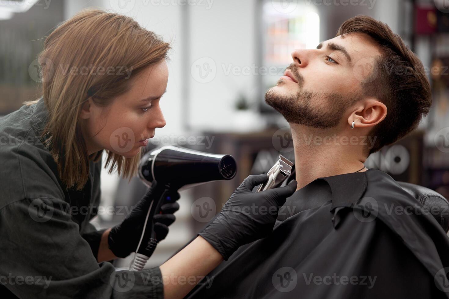 Handsome blue eyed man sitting in barber shop. Hairstylist Hairdresser Woman cutting his hair. Female barber. photo