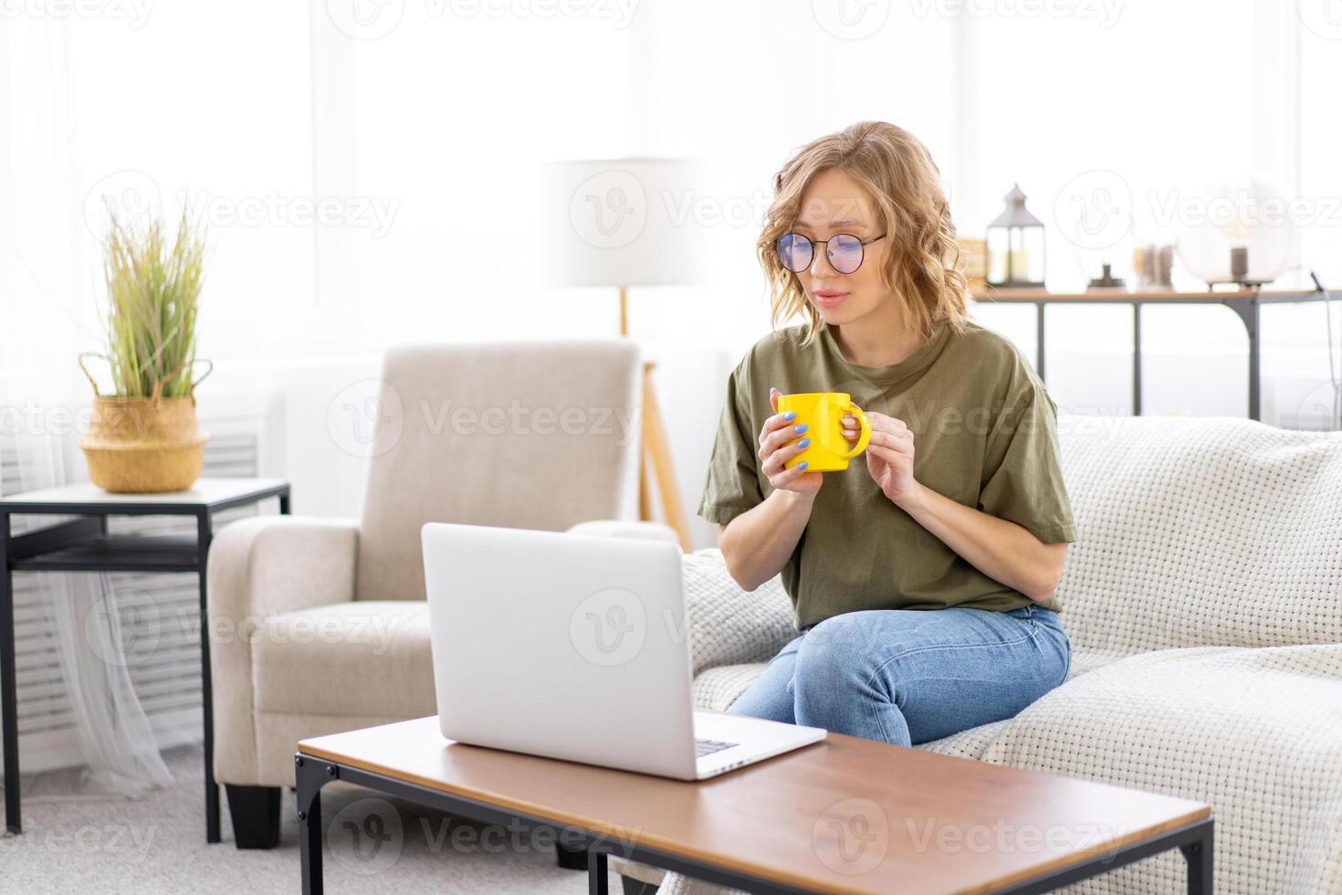 Woman glasses using laptop computer while sitting sofa with big window on background at home interior photo