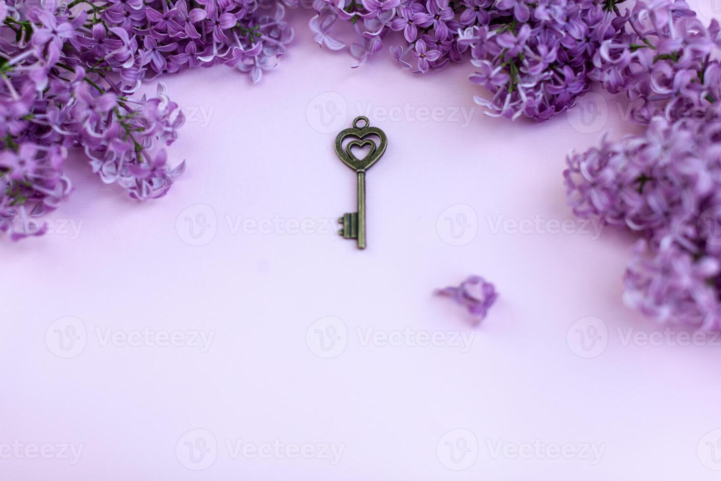 Blank paper card with lilac flowers and vintage key on pink background. Space for text. Flat lay style. photo