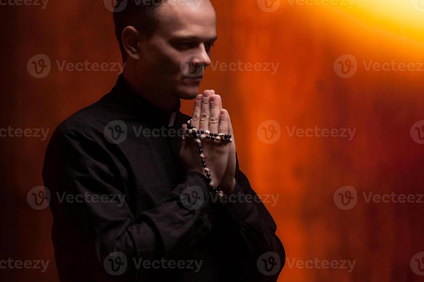 Portrait of handsome catholic priest or pastor with dog collar, dark red background. photo