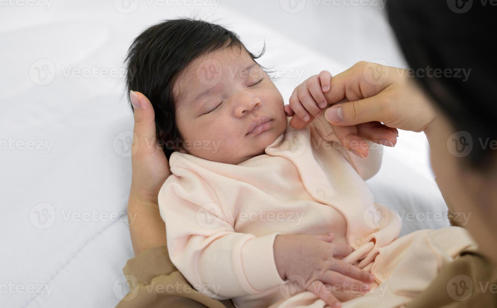 Mother touching cheek of newborn baby daughter on bed at home. Infant girl or boy sleeping on mom arm. Love and new life concept photo