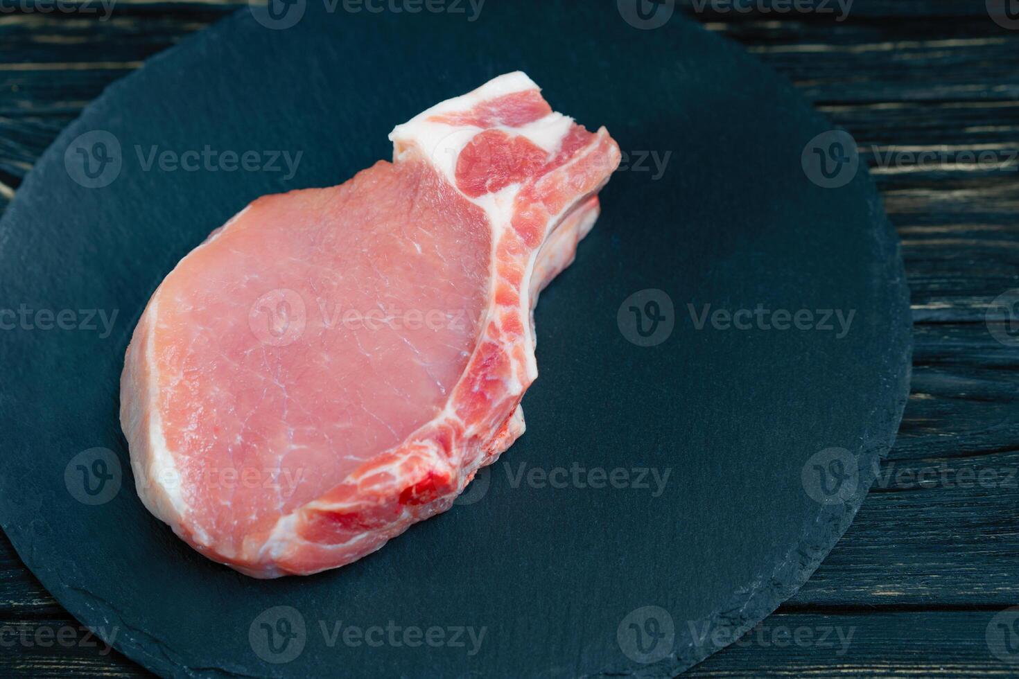 Top view of one pieces raw pork chop steaks on a black stone cutting board. photo