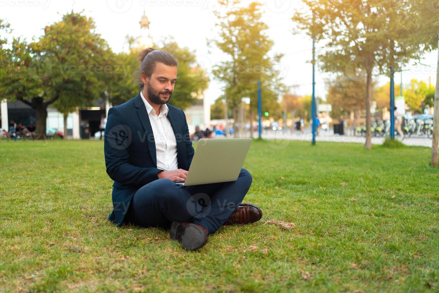 Handsome hispanic male businessman sitting lotus position in public park use laptop photo