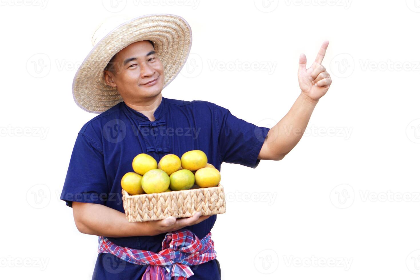 Handsome Asian man farmer wears hat, blue shirt, holds basket of organic orange fruits, point finger up, isolated on white background. Concept, Agriculture occupation, produce crops to market. photo