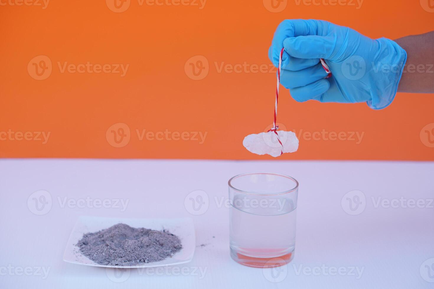 Hand wears blue glove hold alum stone to do science experiment  on glass of water and tray of ash about sedimentation by using alum stone with ash water in glass.Concept, Education, Science lesson. photo