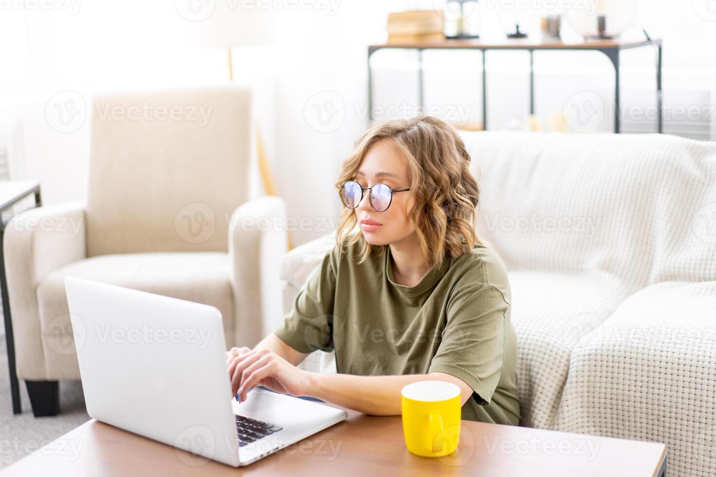 Woman glasses using laptop computer while sitting near sofa with big window on background at home interior photo