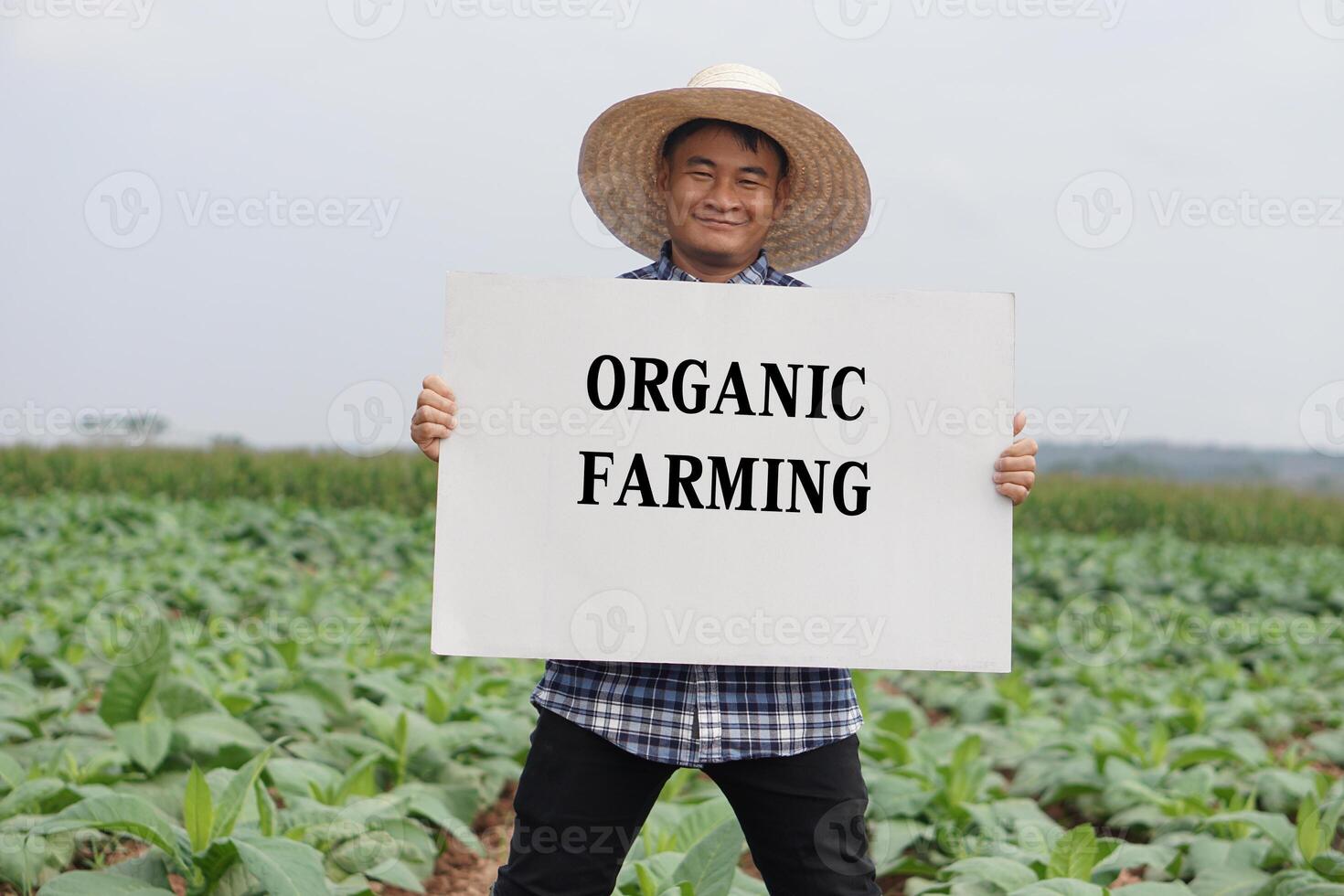 Happy Asian farmer holds paper poster with text Organic Farming in garden. Concept, campaign to do organic agriculture, no pesticide and herbicide or chemicals. Safe crops for health photo