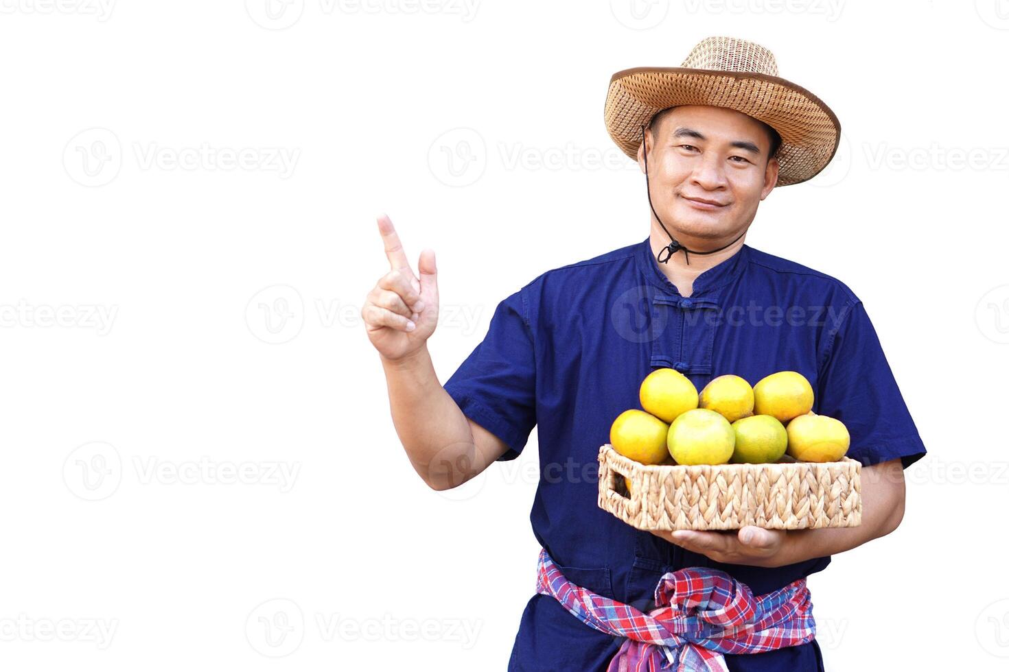 Handsome Asian man farmer wears hat, blue shirt, holds basket of organic orange fruits, point finger up, isolated on white background. Concept, Agriculture occupation, produce crops to market. photo