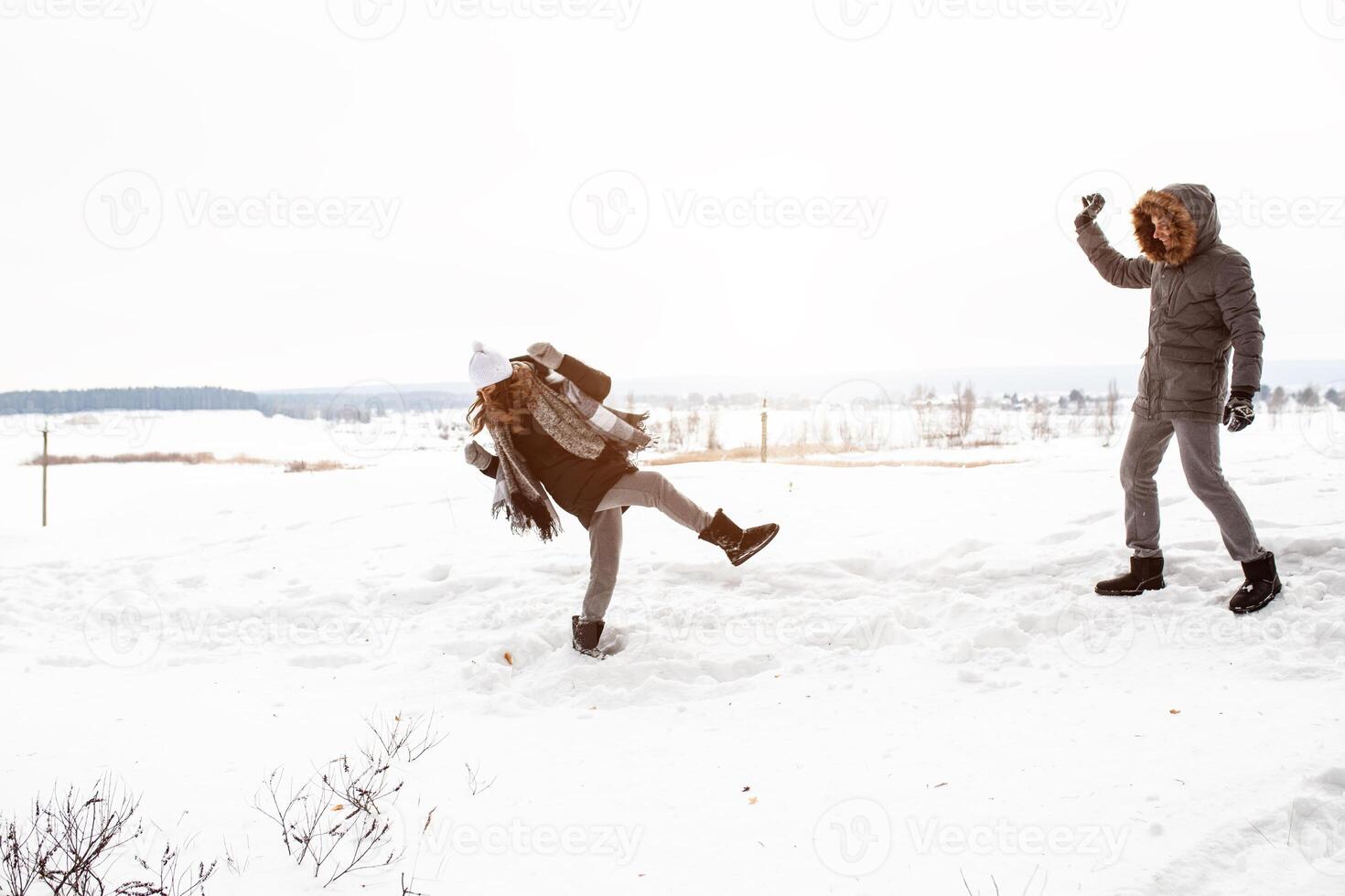 Carefree happy young couple having fun together in snow in winter woodland throwing snowballs at each other during a mock fight photo