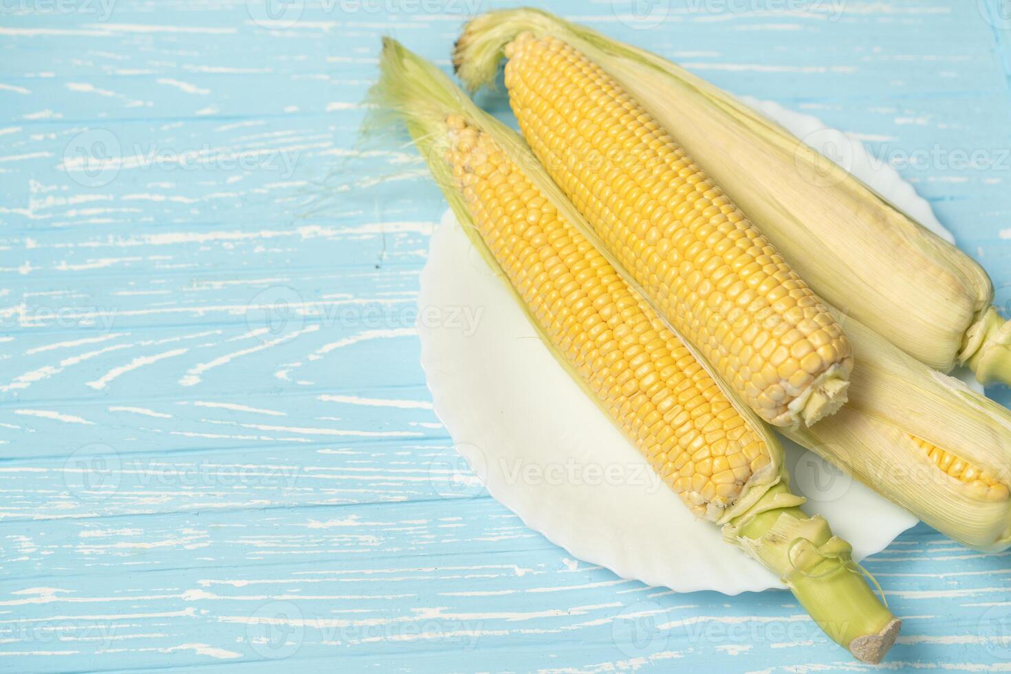 Corn cob with green leaves lies on white plate blue color background. photo