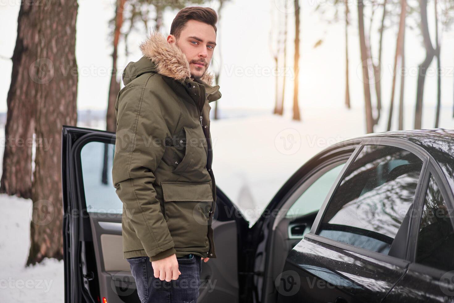 Attractive Caucasian man stands in winter forest near his car. photo