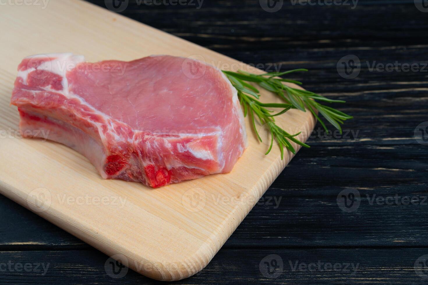 Top view of one pieces raw pork chop steaks with rosemary on a cutting board. photo