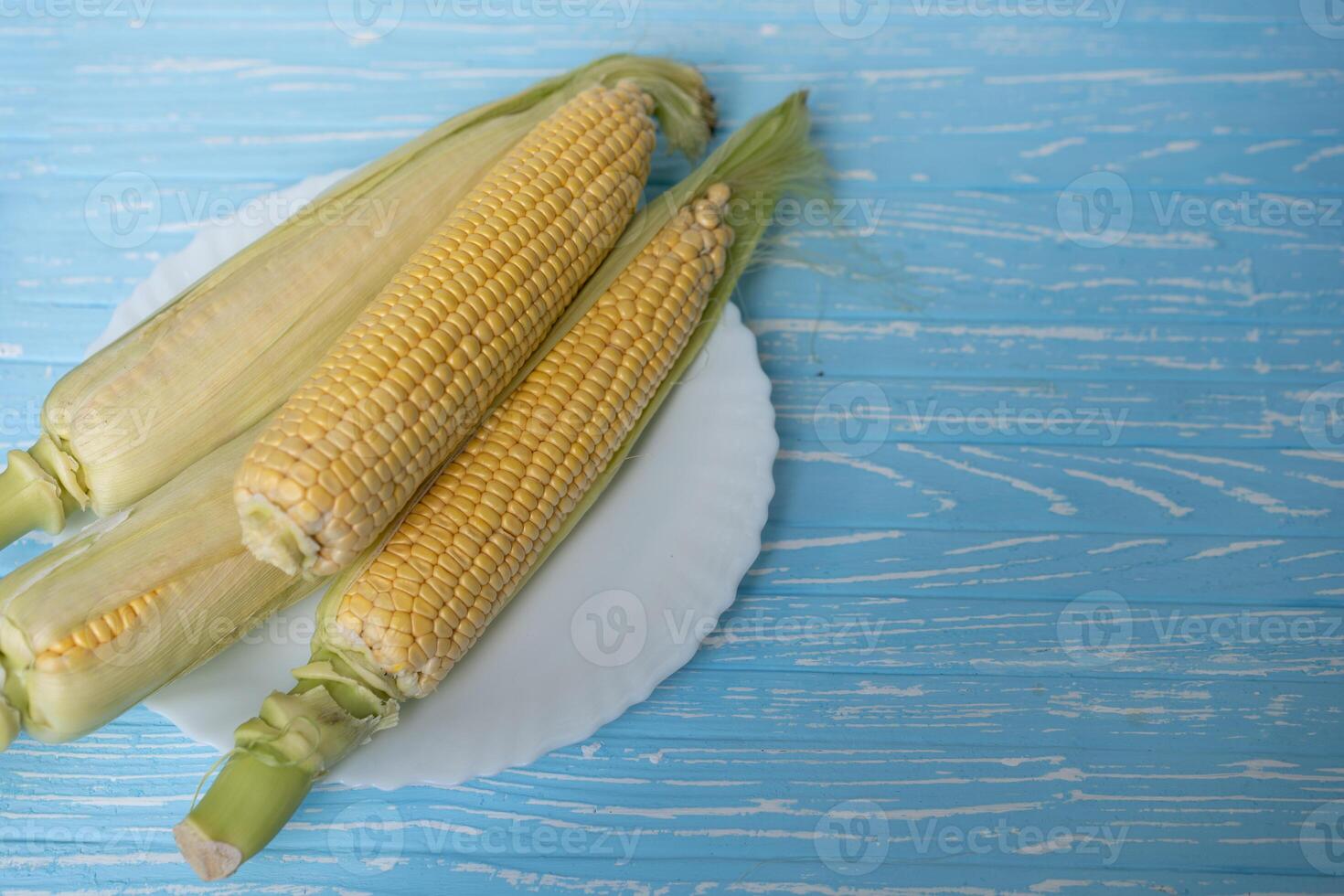 Corn cob with green leaves lies on white plate blue color background. photo