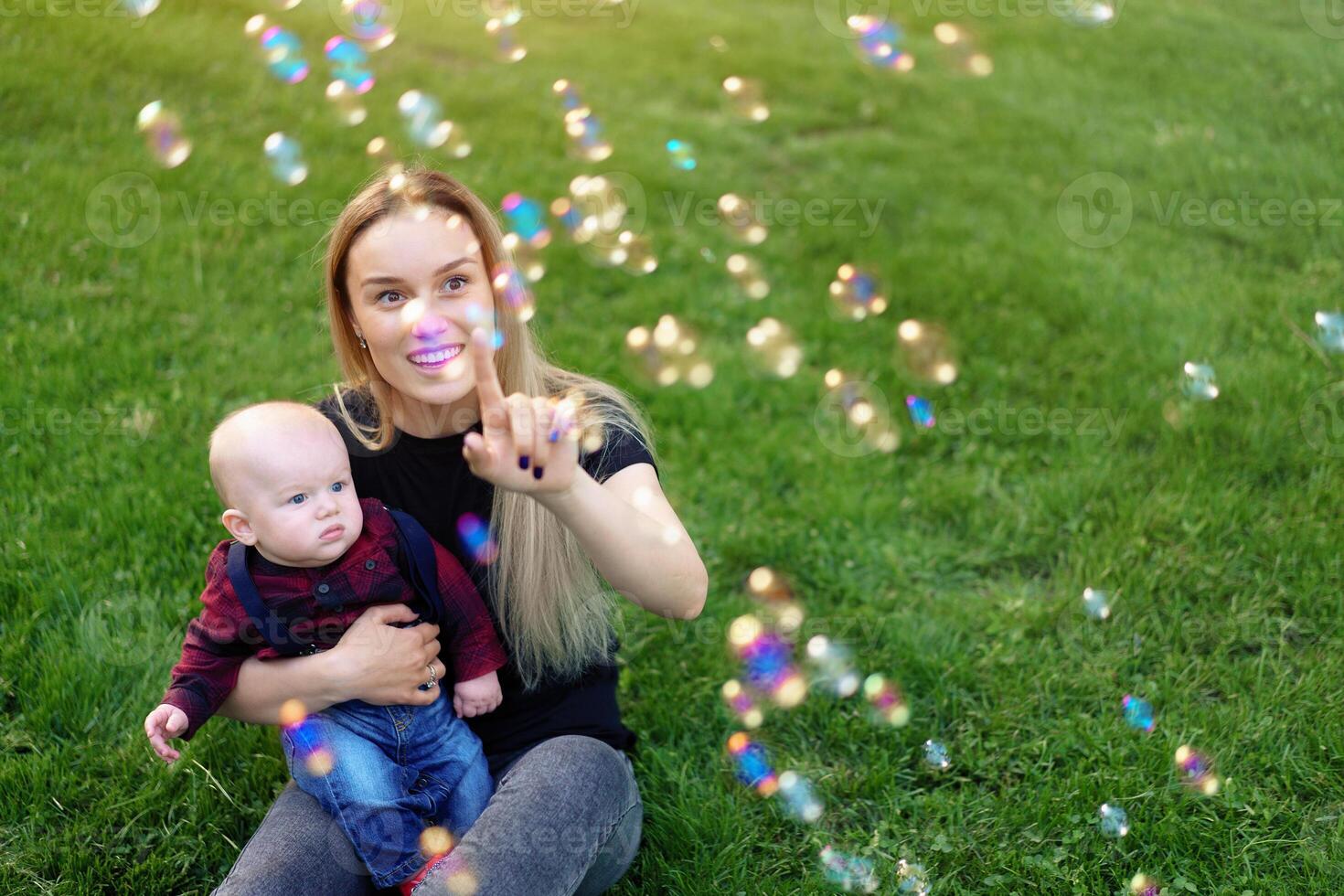 Young Caucasian mother inflates soap bubbles with her little son in a park on a sunny summer day. photo