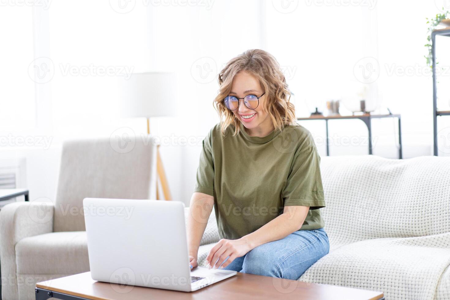 Woman glasses using laptop computer while sitting sofa with big window on background at home interior photo