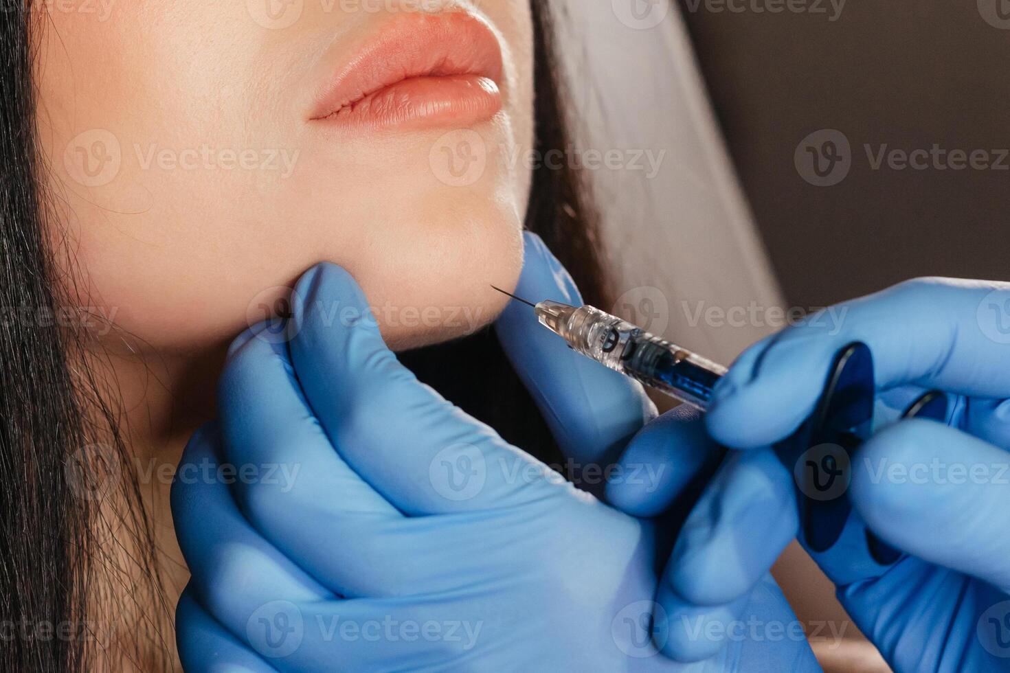 Closeup of young woman receiving injection in beauty salon. Cosmetology. Filler injection chin make chin longer photo