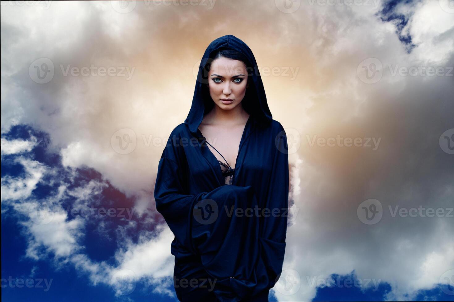 A woman is a prophet sorcerer and a preacher in a black mystical cloak with a hood against a dramatic background... photo