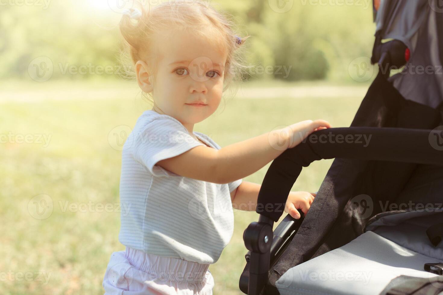 Baby girl standing near a baby carriage photo