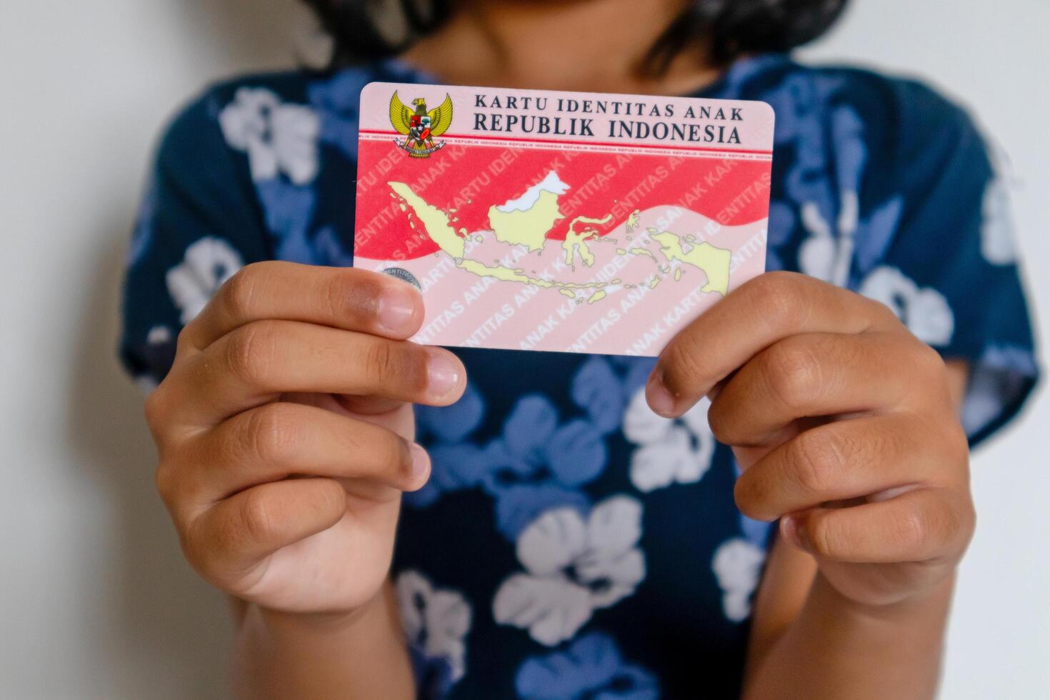 Jakarta, Indonesia, 2024 - A little girl in blue dress holding The Indonesian child identity card or Kartu Identitas Anak photo