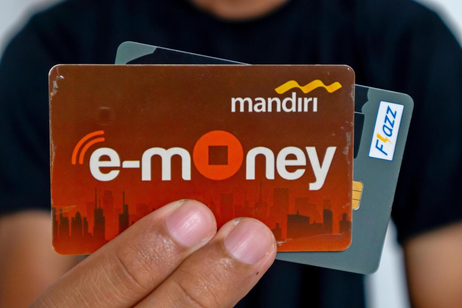 Jakarta, Indonesia, 2024 - A man in black clothes holding the electronic money cards or multifunctional transaction card with RFID Chip Technology for non-cash payment photo