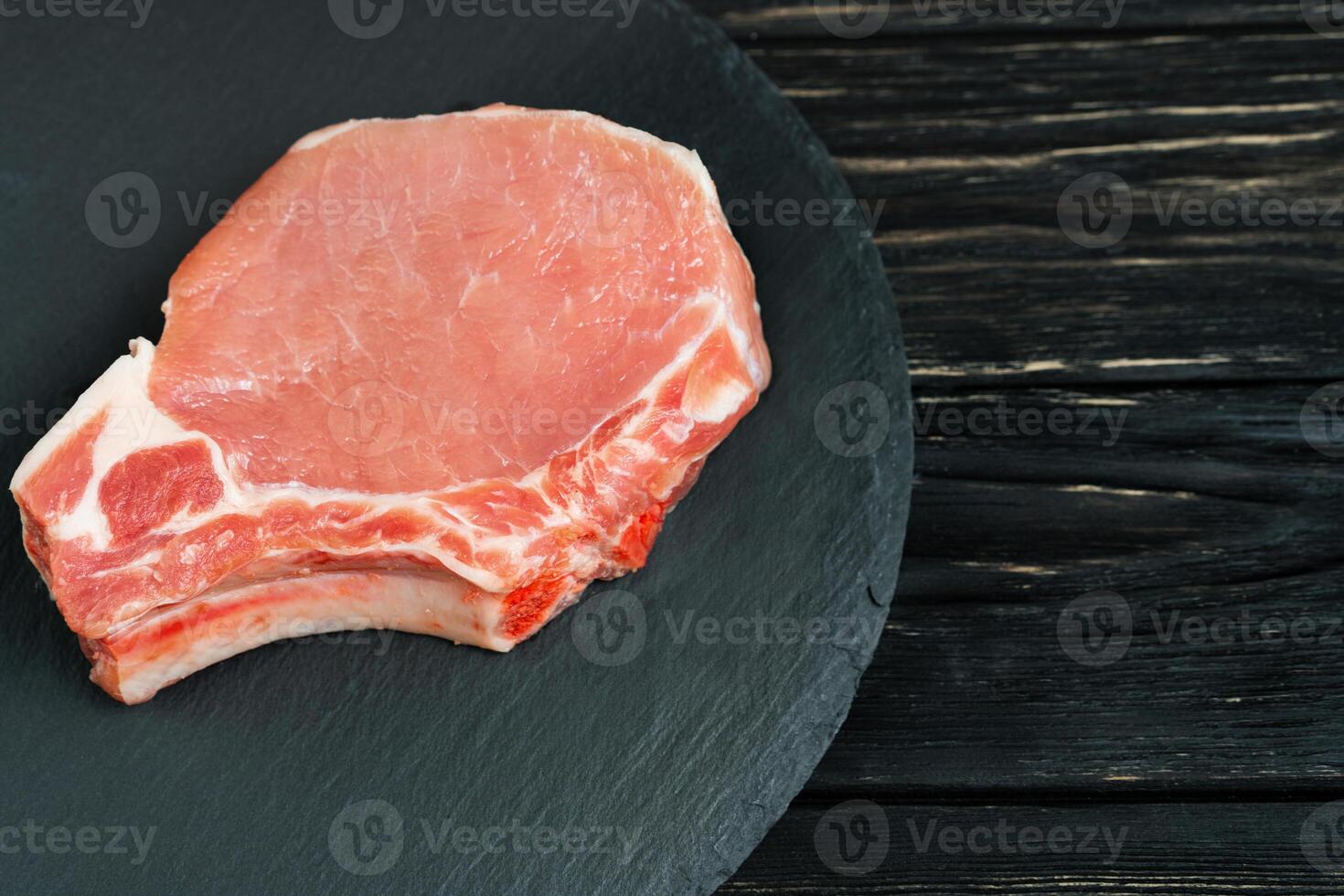 Top view of one pieces raw pork chop steaks on a black stone cutting board. photo