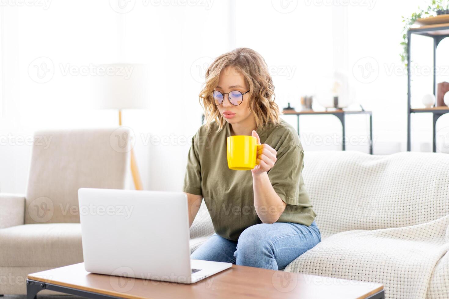 Woman glasses using laptop computer while sitting sofa with big window on background at home interior photo