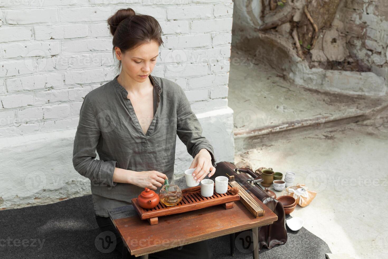 oriental Maestro de té ceremonia con blanco ladrillo pared en el antecedentes. tradicional té fiesta en el naturaleza con mujer vestido en el gris camisa foto