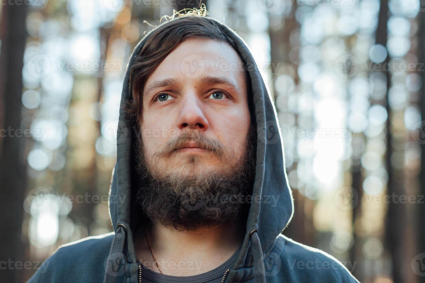 close up portrait of a bearded hipster tourist in gray hood man in the sunlight woods forest photo