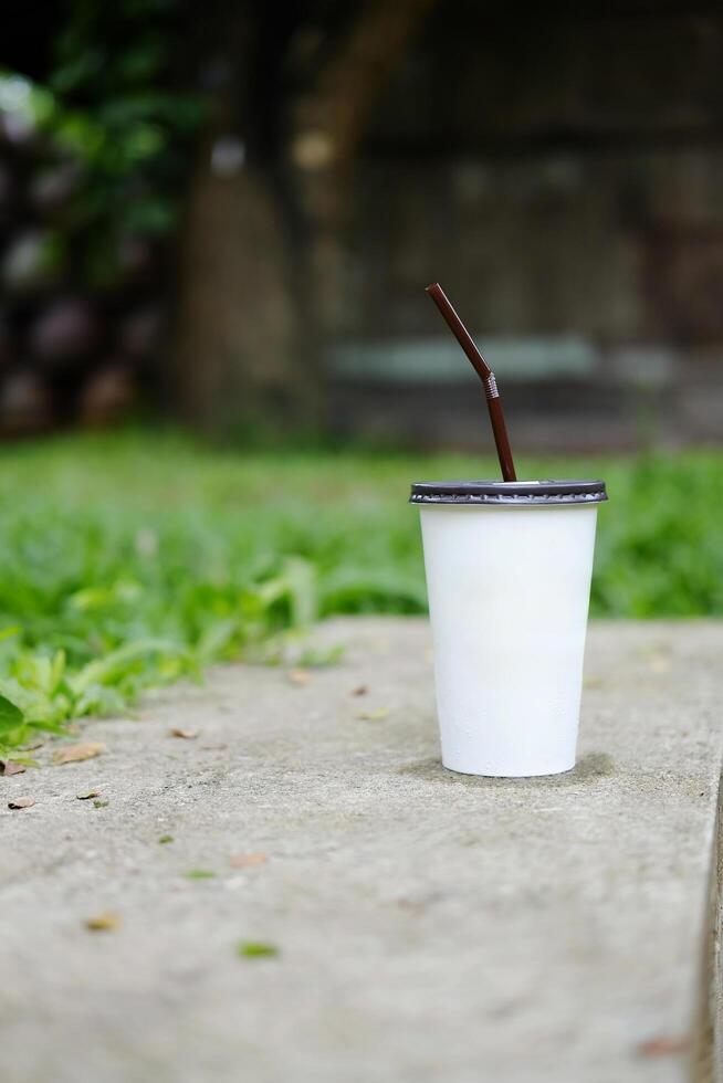 papel vaso de con hielo café en hormigón paso piso con césped campo en tropical jardín de café foto