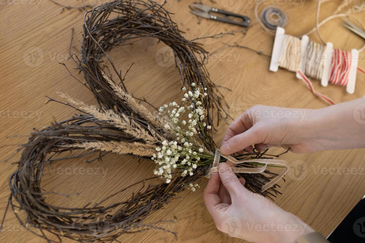 Hands tying bow on wicker wreath of birch branches on wooden background, handmade decoration photo