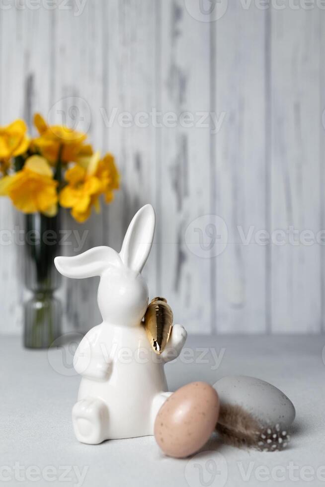 Easter bunny and eggs on table, bouquet of daffodils on background. Copy space photo