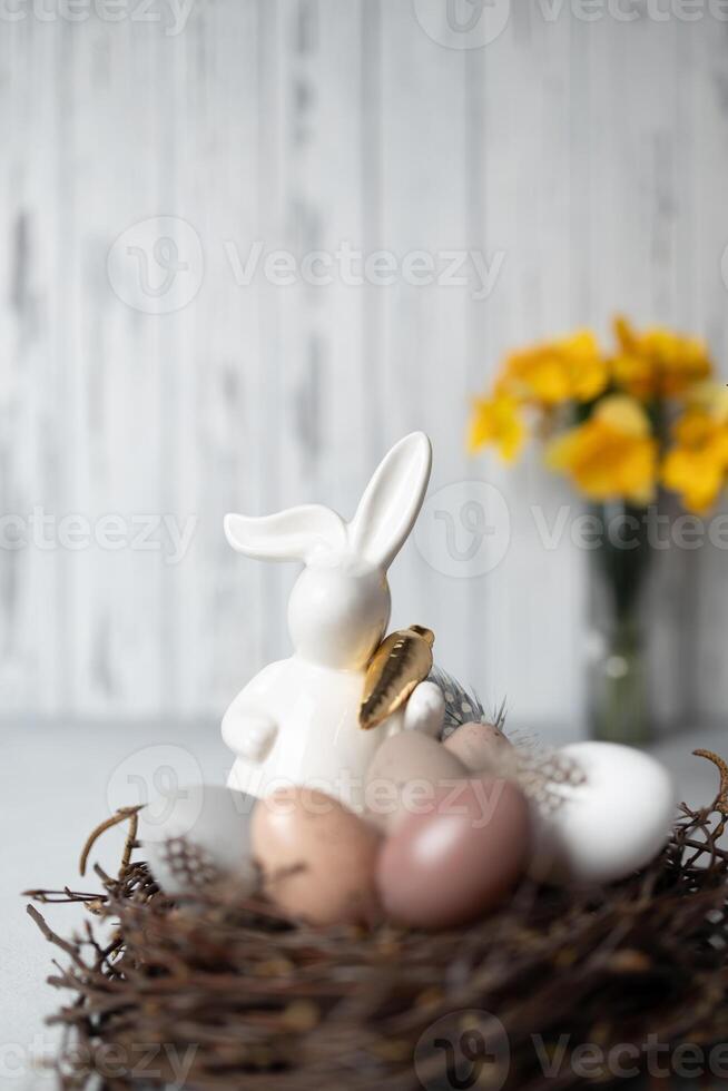 Easter bunny and eggs in nest of birch branches. Bouquet of daffodils on background. Copy space photo