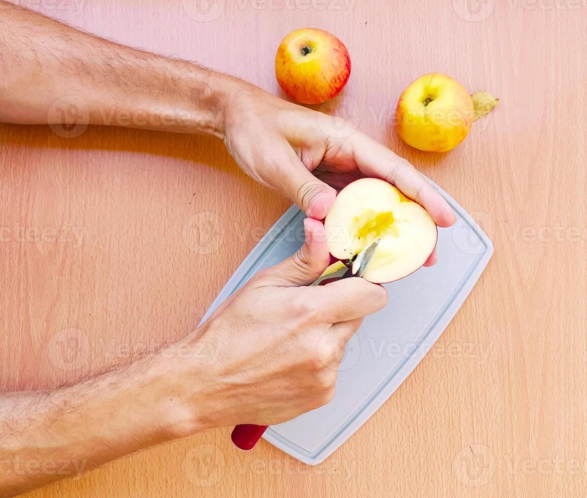 Close up male hands cut an apple into slices. Top view of preparing fruits over kitchen table. photo