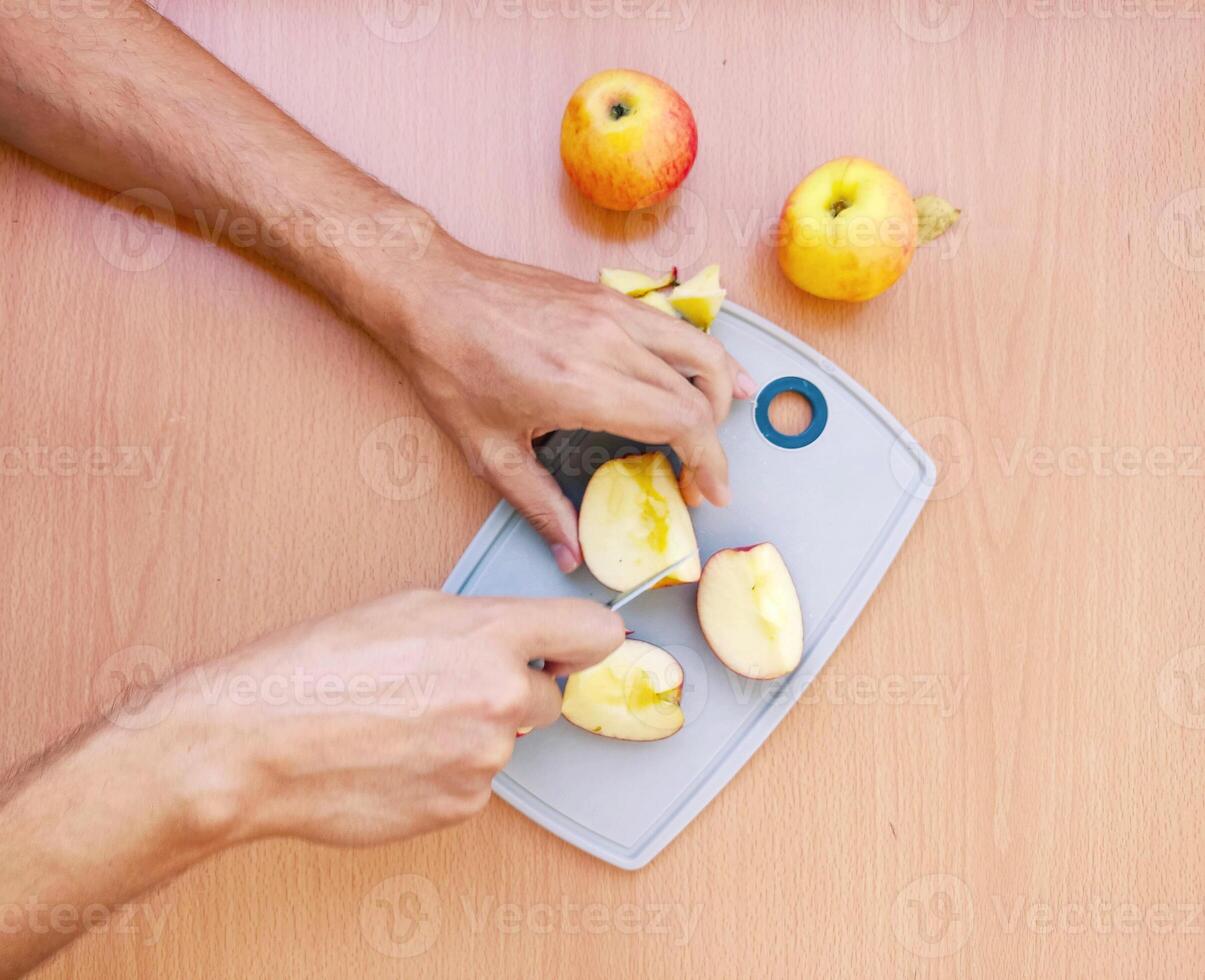 Close up male hands cut an apple into slices. Top view of preparing fruits over kitchen table. photo