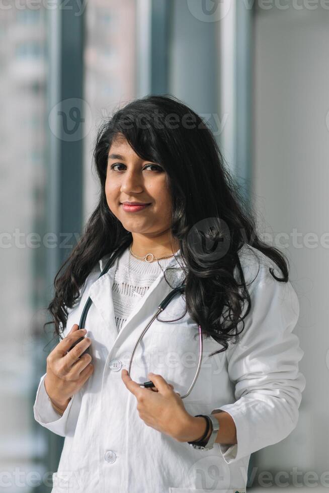 joven indio médico estudiante a el clínica en práctica. hembra médico en un blanco Saco con un estetoscopio foto