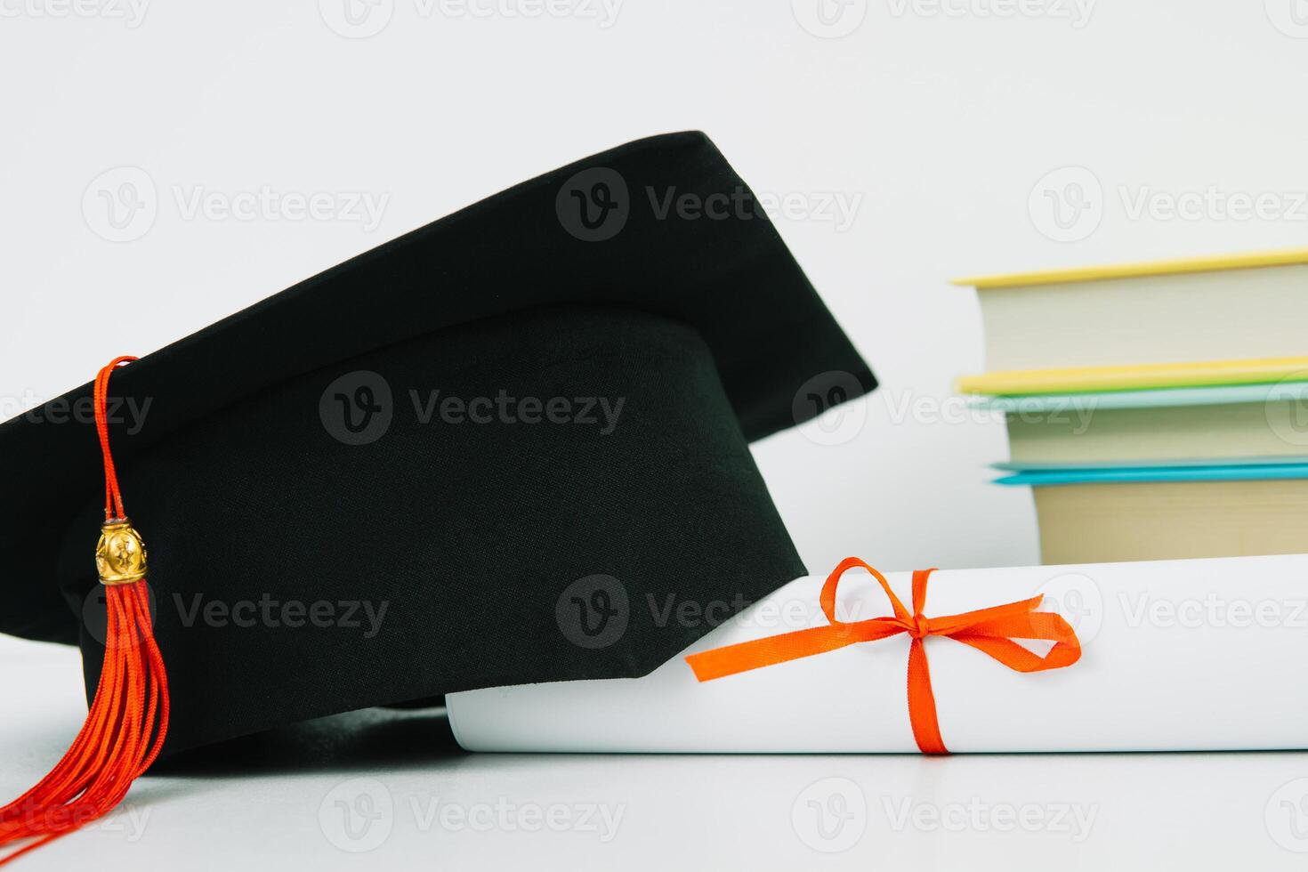 A black square graduate hat with a red tassel lies on a diploma and a stack of books. Education concept photo