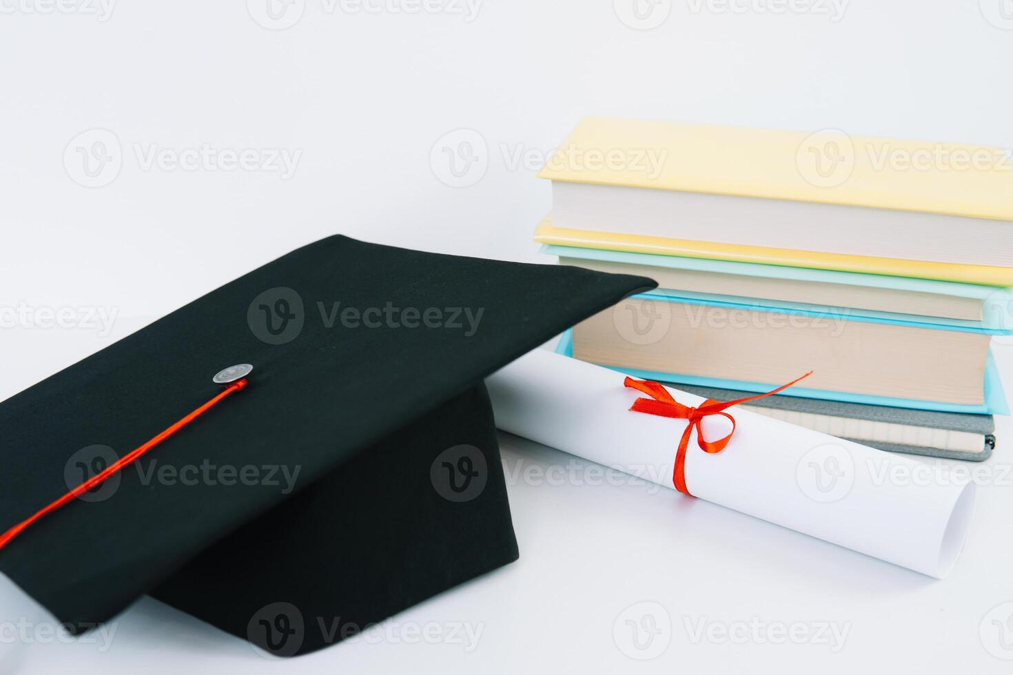 A black square graduate hat with a red tassel lies on a diploma and a stack of books. Education concept photo