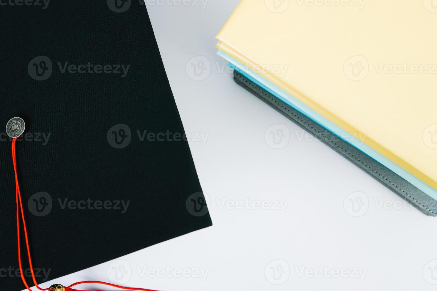 A black square graduate hat with a red tassel lies on a diploma and a stack of books. Education concept photo