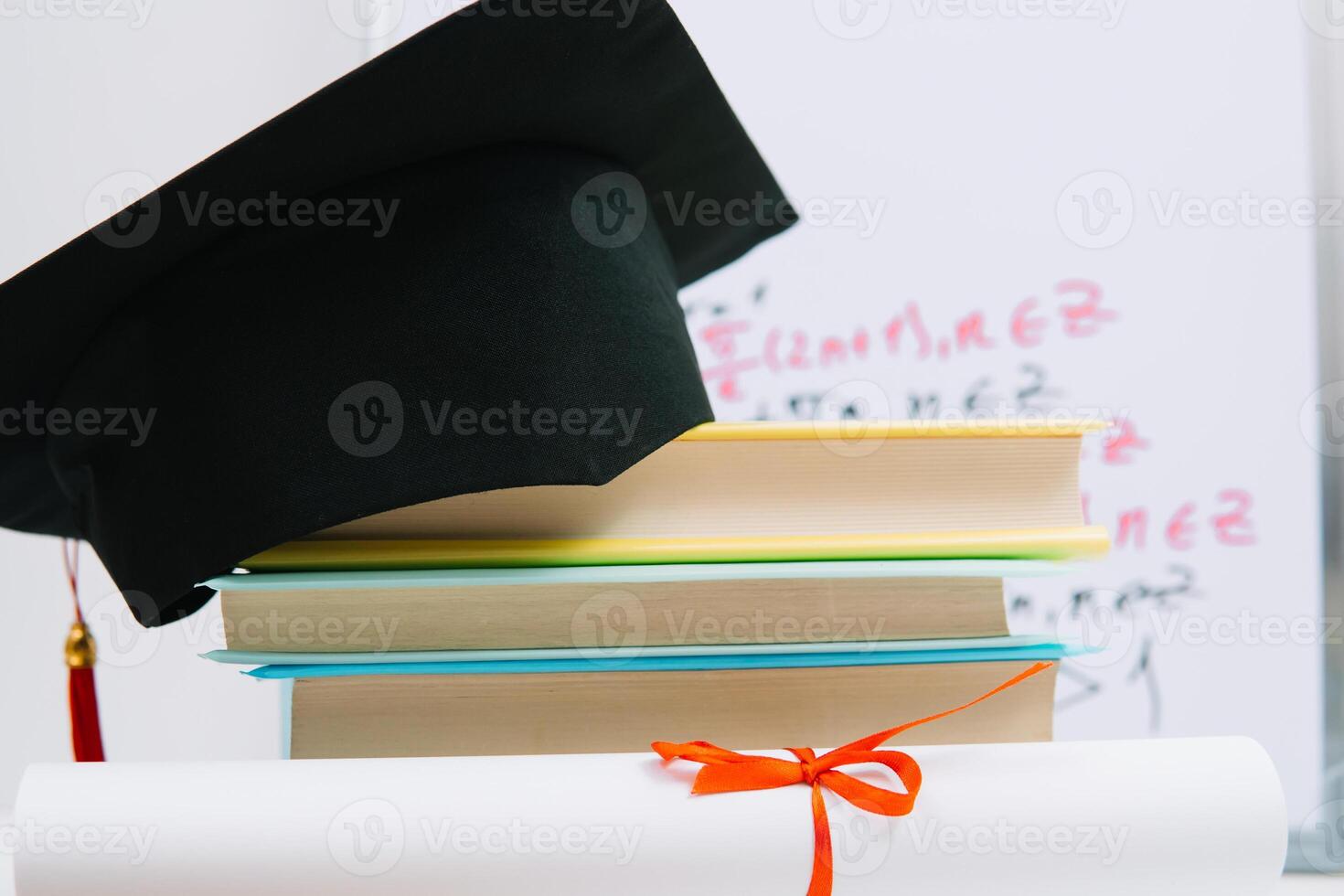 A black square graduate hat with a red tassel lies on a diploma and a stack of books. Education concept photo