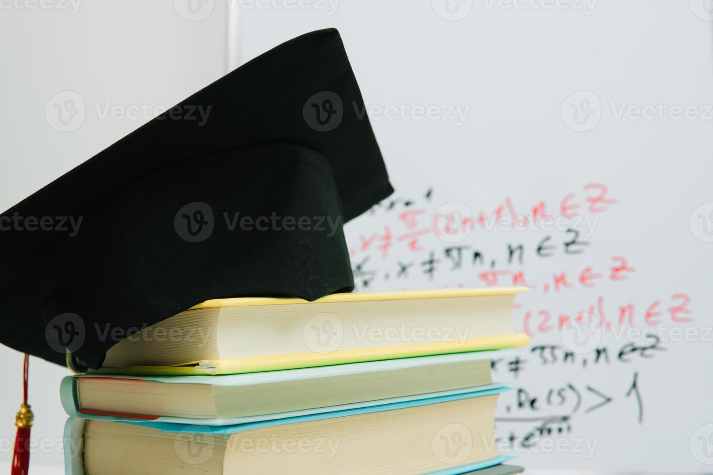 A black square graduate hat with a red tassel lies on a stack of books photo