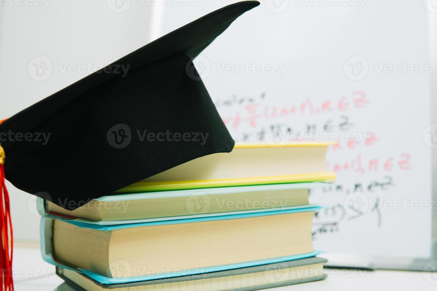 A black square graduate hat with a red tassel lies on a stack of books photo