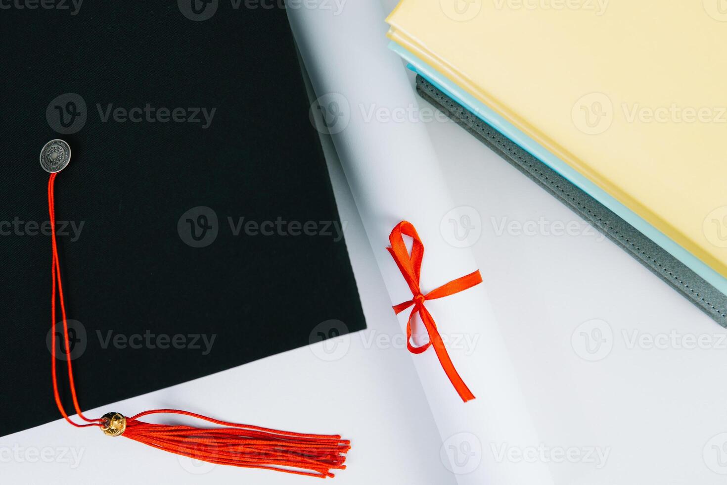 A black square graduate hat with a red tassel lies on a diploma and a stack of books. Education concept photo