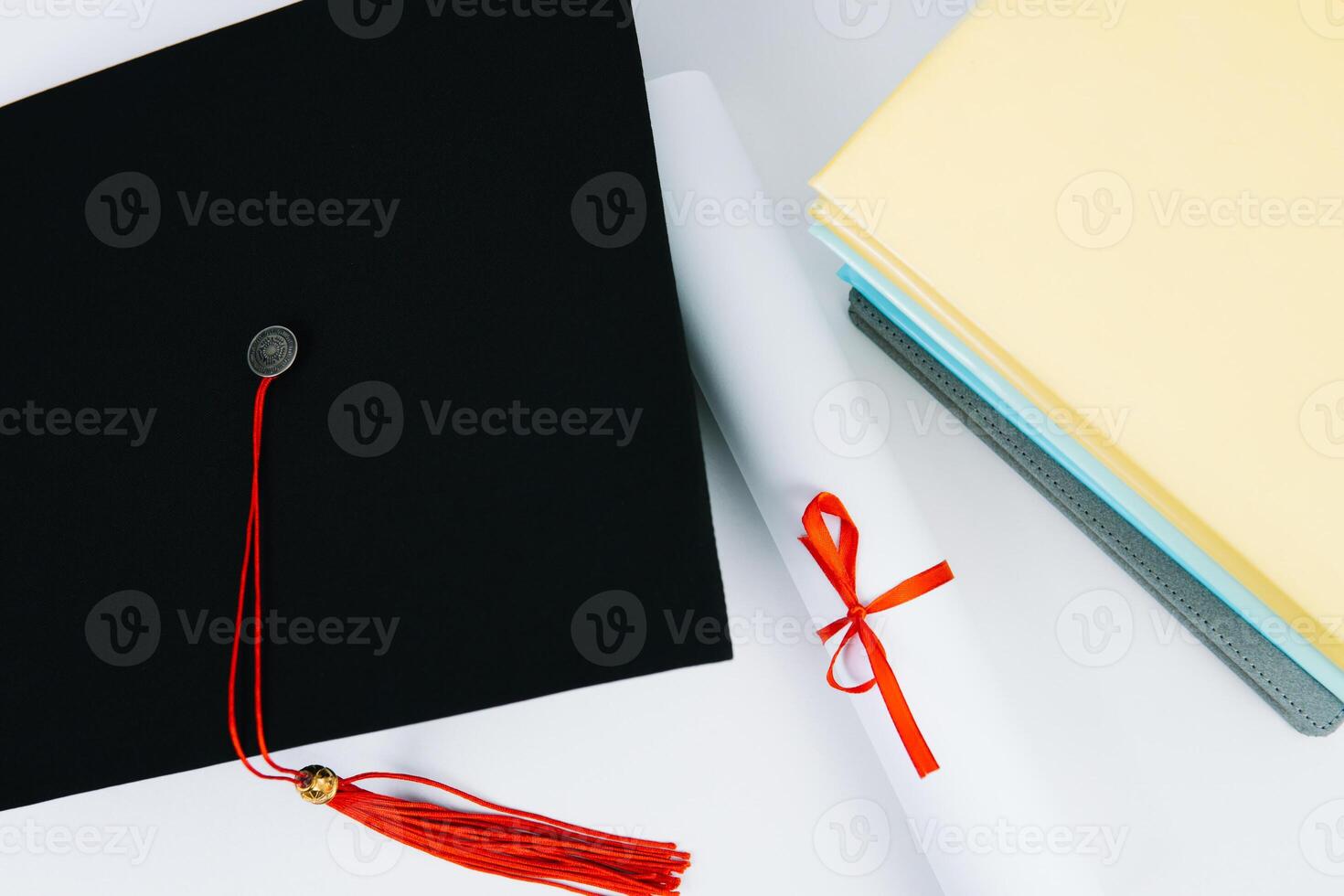A black square graduate hat with a red tassel lies on a diploma and a stack of books. Education concept photo