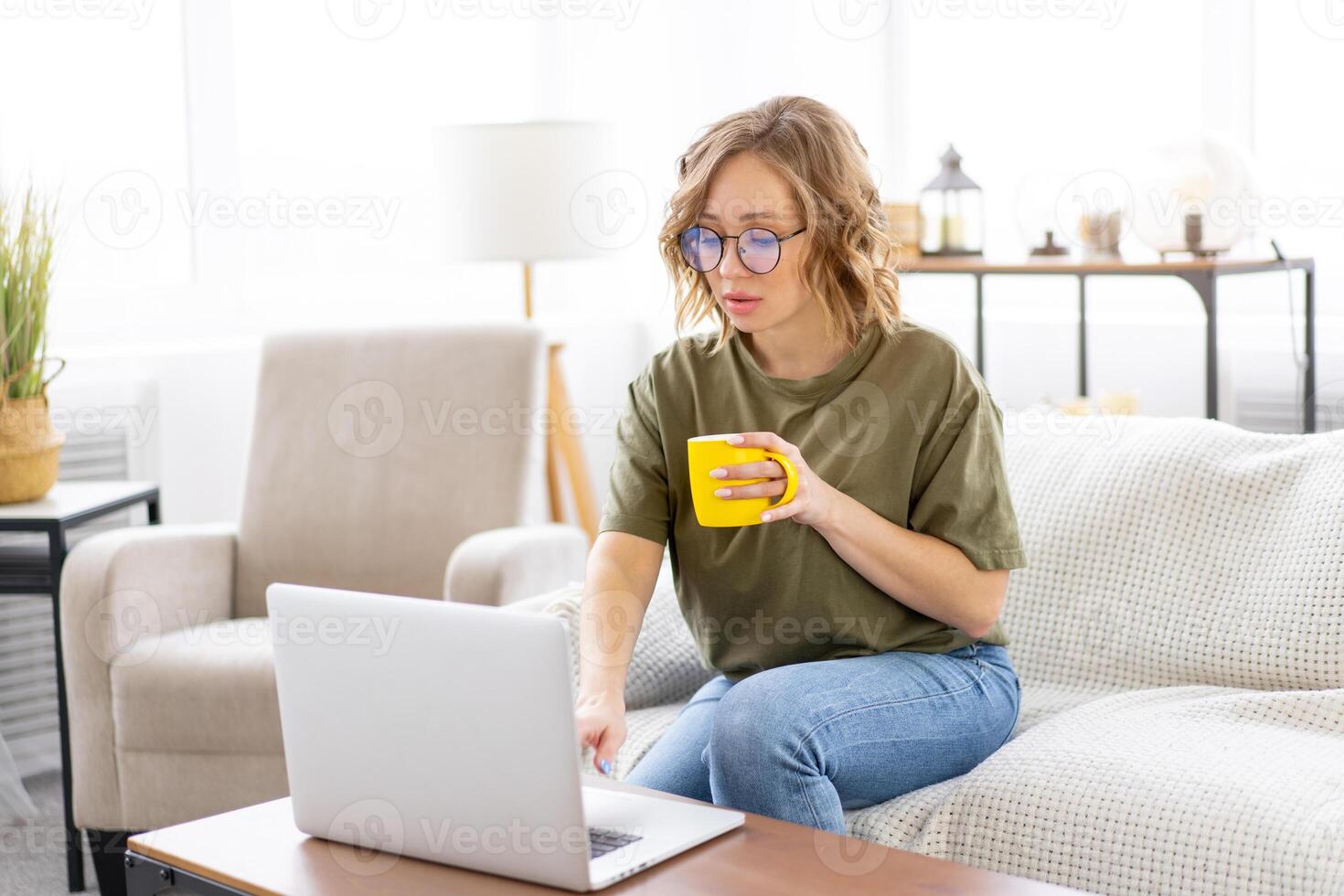Woman glasses using laptop computer while sitting sofa with big window on background at home interior photo