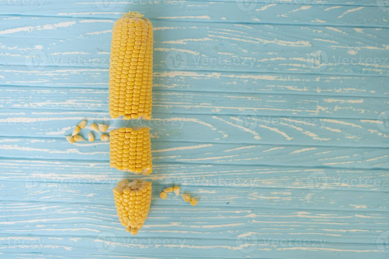 Corn cob with green leaves lies on table blue color background. photo